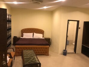 A bedroom with a tufted headboard bed, a small table, and a mirror.