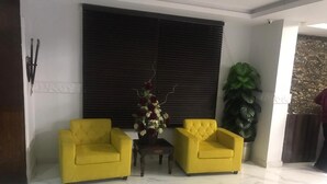 A room with two yellow armchairs, a small table, and a large window with blinds. - National City Hotel (Rawalpindi)