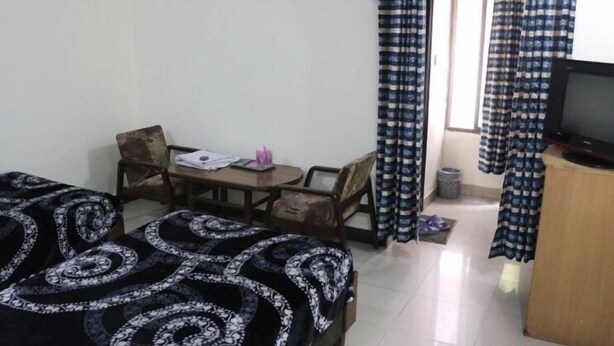 A small, tidy room with a bed, a desk, a chair, a television, and a window with curtains.