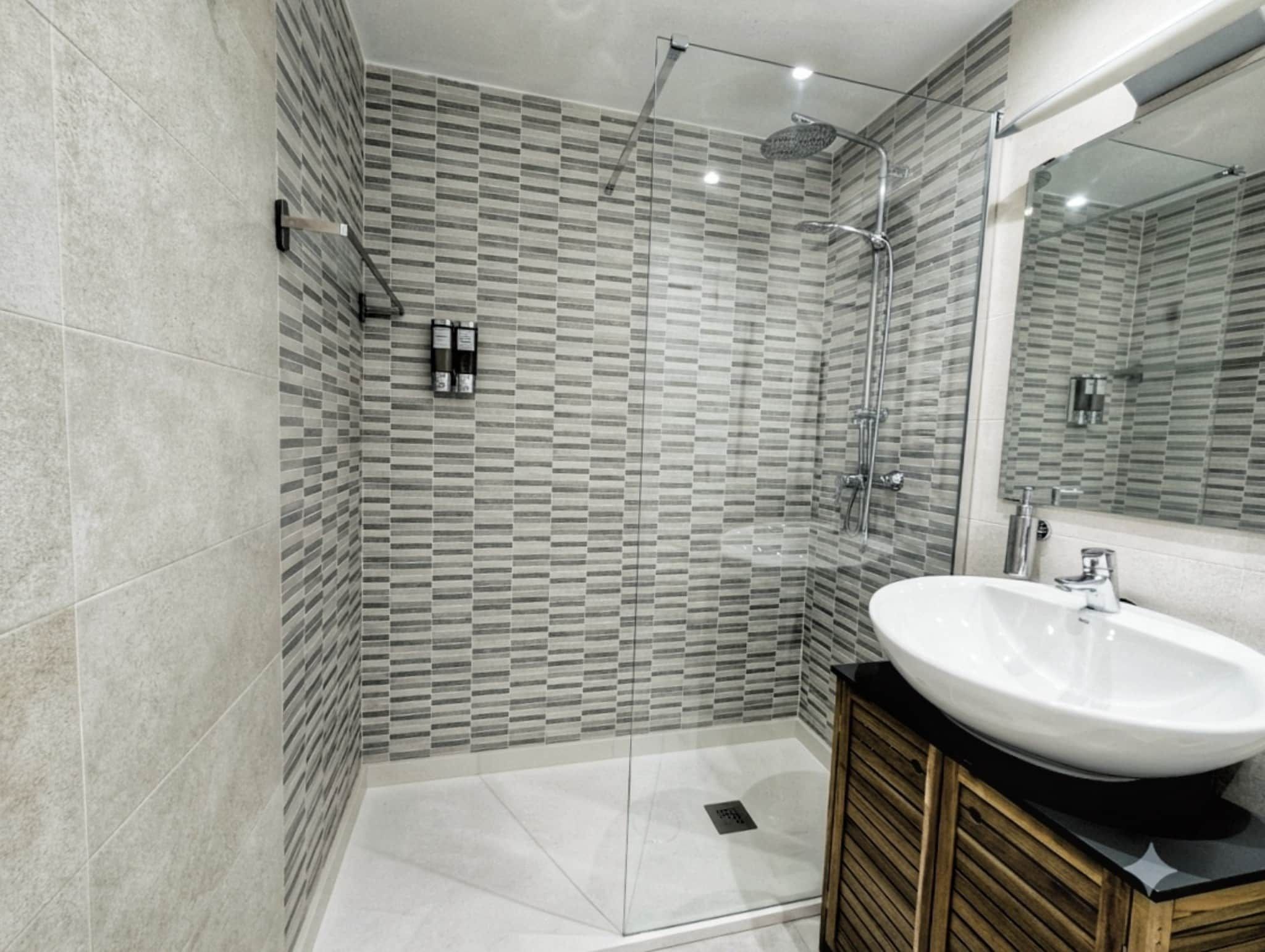 Een moderne badkamer met een douchecabine van glas, een groot wastafelmeubel en een houten wastafel.