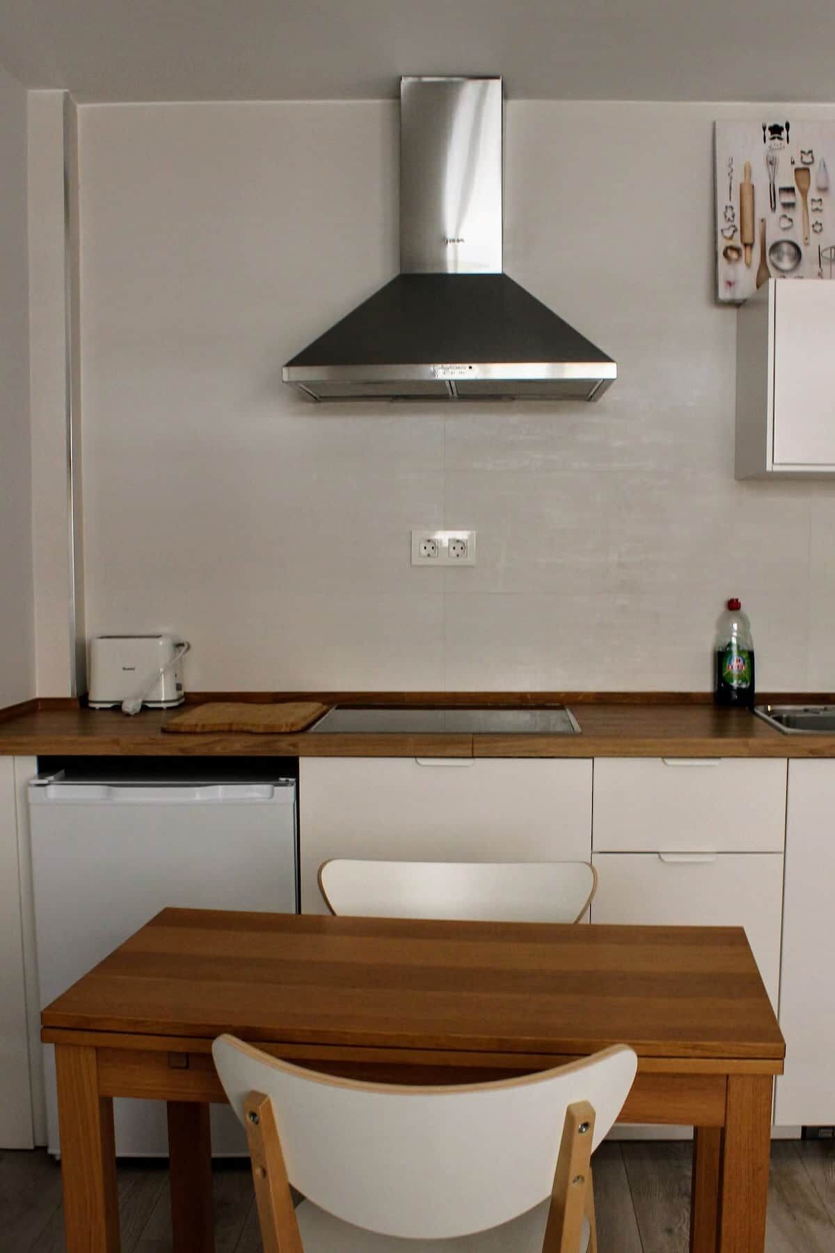 Een moderne keuken met een roestvrijstalen afzuigkap, een houten aanrecht, een witte stoel en een klein wit kastje.