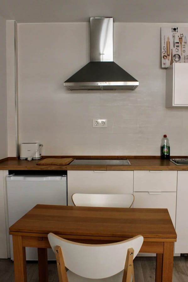 A modern kitchen with a stainless steel range hood, a wooden countertop, a white chair, and a small white cabinet.