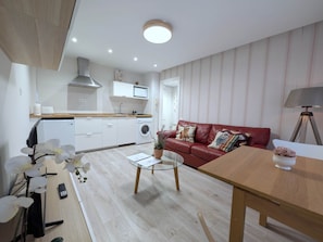 A compact living space with a kitchenette, a red leather sofa, a glass coffee table, and a lamp.