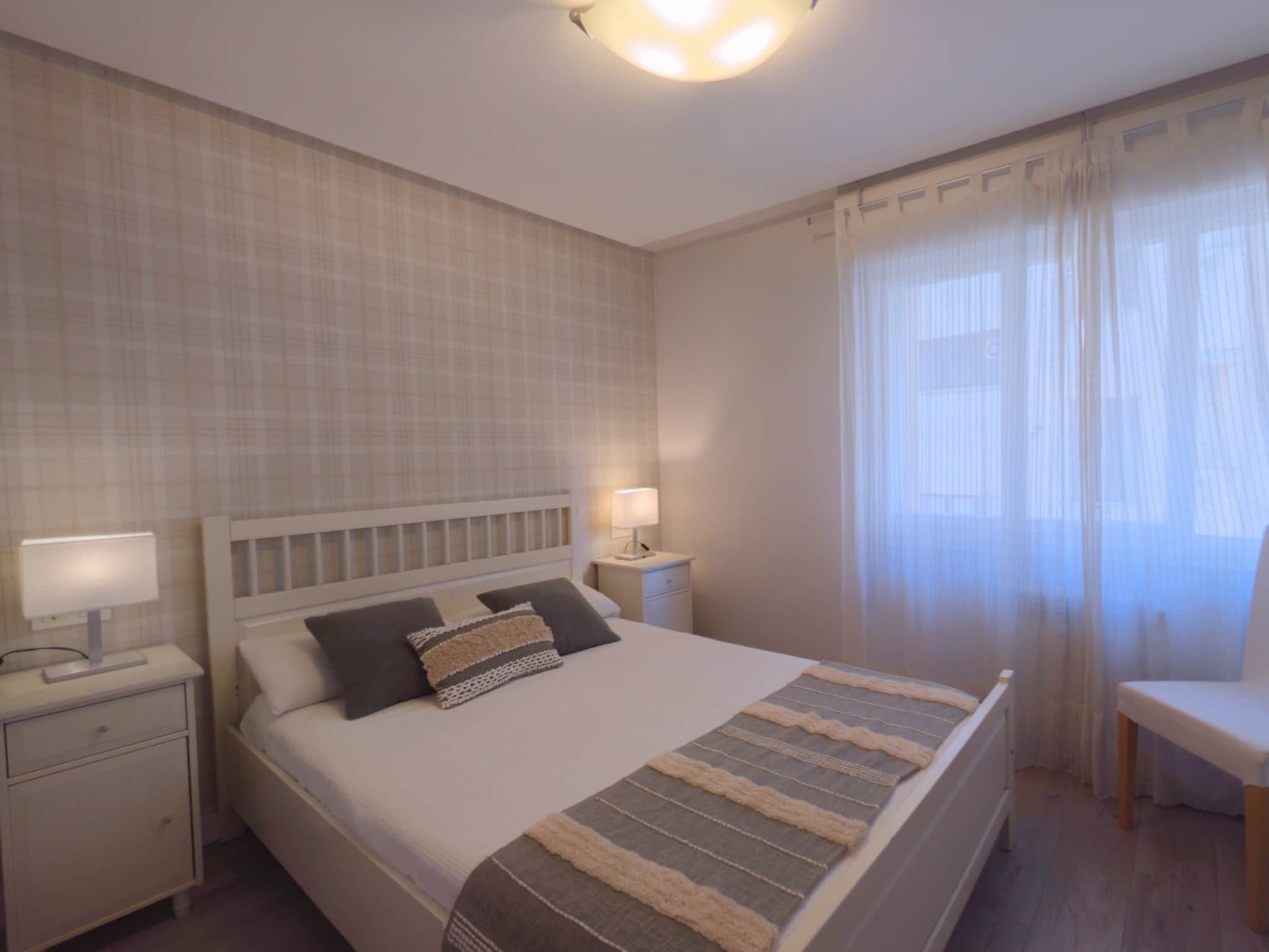 Een hotelkamer met een bed, nachtkastjes, een lamp, een stoel en een raam met gordijnen.
