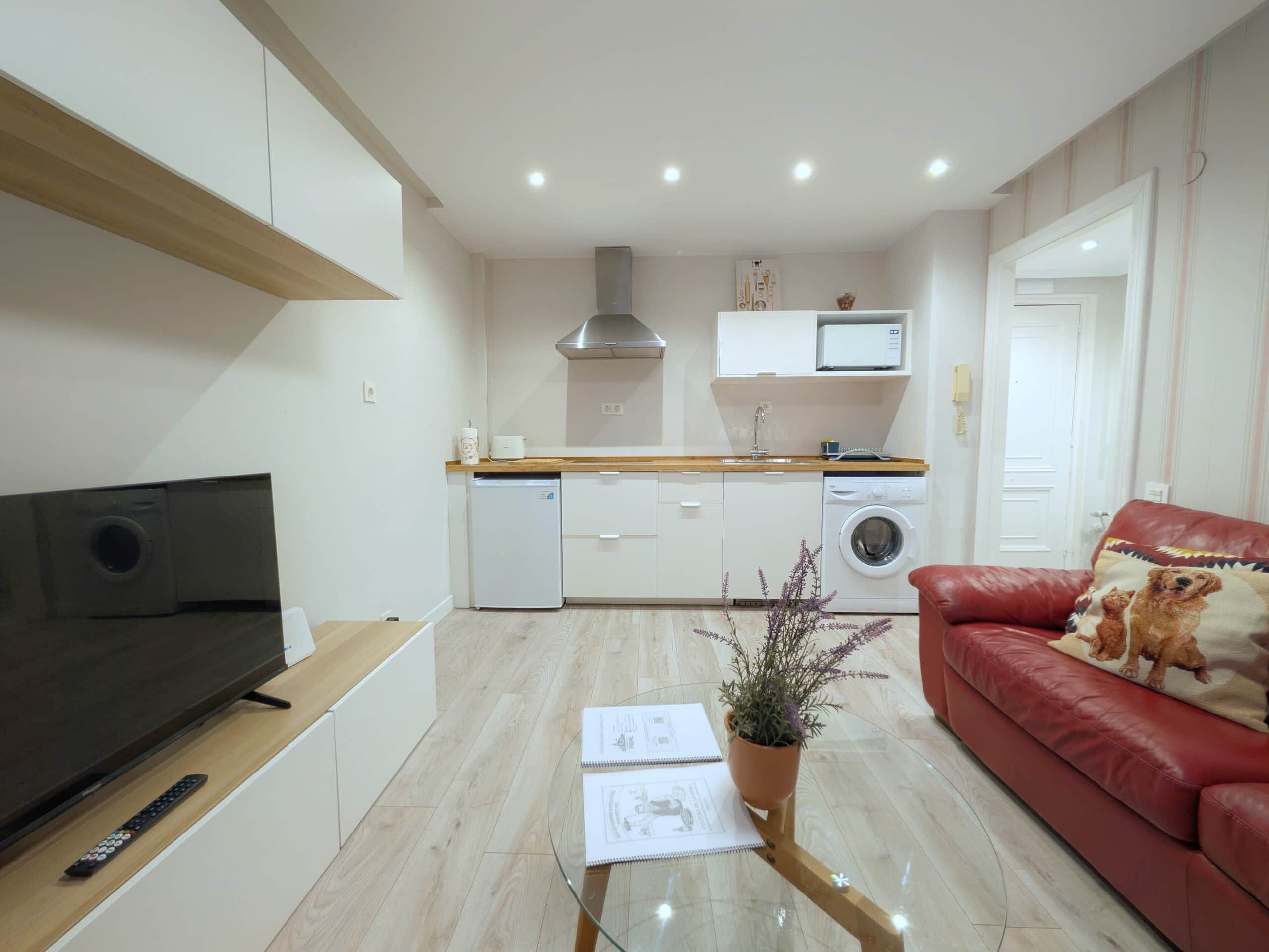 Un appartement moderne comprenant une cuisine, un espace de vie avec un canapé rouge, une télévision et une table basse en verre.