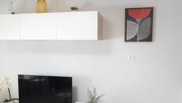 Un televisor de pantalla plana sobre un soporte de madera, un mueble blanco encima y una pequeña planta en maceta al lado del televisor.
