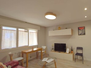 Een woonkamer met een televisie, een eettafel, stoelen, een bank en een glazen salontafel.