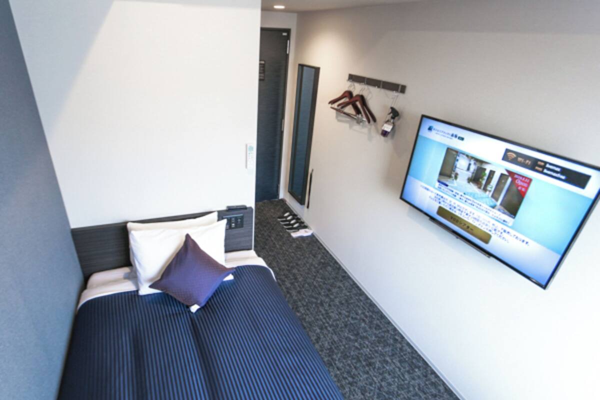 Quarto de hotel moderno com uma cama, televisão presa na parede e um sapateiro.