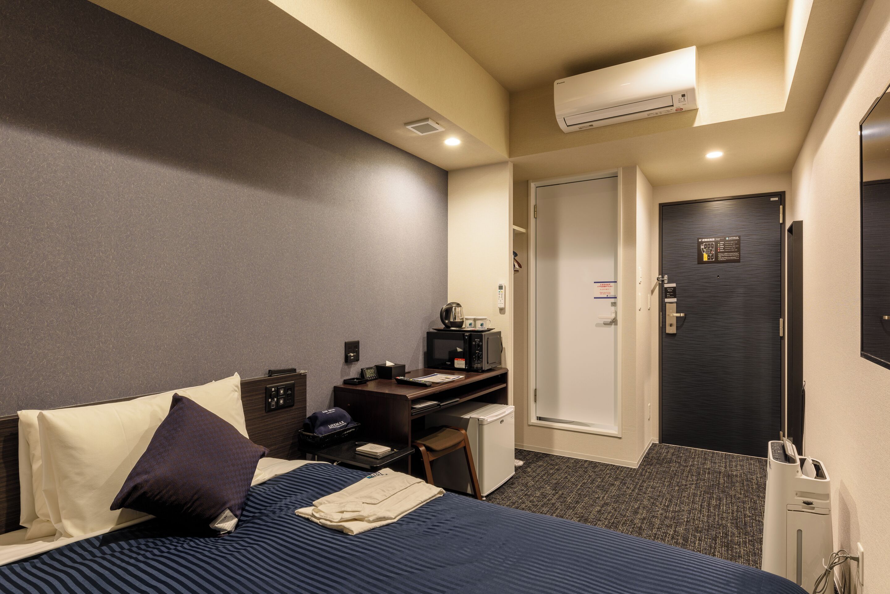 A hotel room with a bed, desk, chair, microwave, and a small refrigerator.