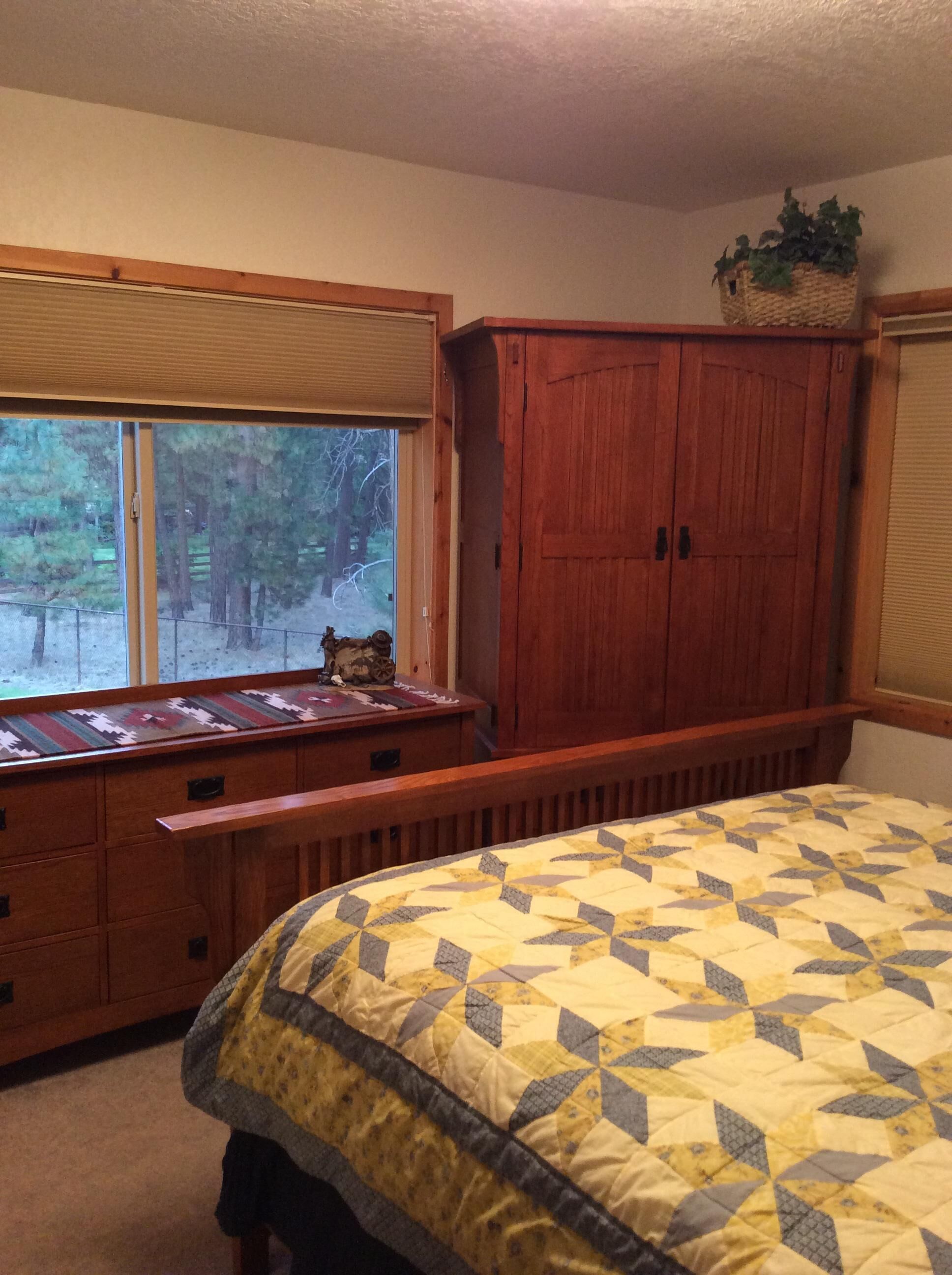 A bedroom with a large bed, a wooden wardrobe, a window with a view of trees, and a bench by the window.