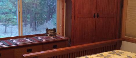 A bedroom with a large bed, a wooden wardrobe, a window with a view of trees, and a bench by the window.