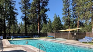 A rectangular swimming pool with clear blue water, surrounded by lounge chairs and a shaded area.