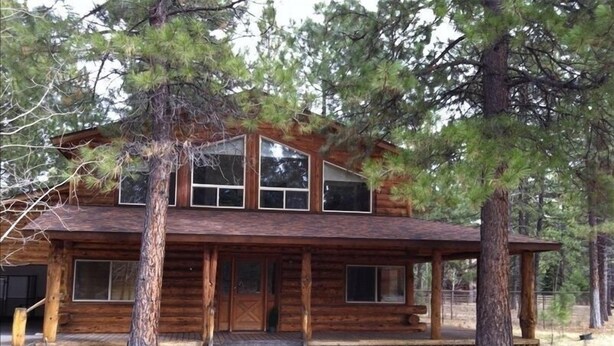 A log cabin with a porch, large windows, and a covered entryway.