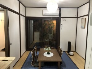 Une pièce de taille modeste, avec une table à manger en bois, des chaises, une petite plante en pot et un tapis bleu sur le sol.