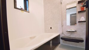 Une salle de bain moderne avec une grande baignoire, une douche et un petit meuble-lavabo avec un miroir.