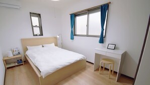 Une chambre à coucher comprenant un lit, un bureau, une chaise, une table de chevet et une fenêtre avec des rideaux.