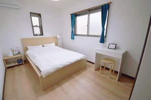 A bedroom with a bed, a desk, a chair, a nightstand, and a window with curtains.