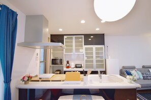 A modern kitchen with white cabinets, a microwave, and a coffee maker. There is a dining table with a laptop and a vase of flowers.