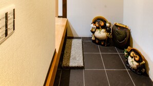 Kapea käytävä, jossa on perinteinen puinen kattorakenne, pieni puinen rakennuksen pienoismalli, kehystetty maalaus ja kaksi keramiikkapenguiinia lattialla.