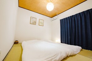 A hotel room with a bed, a ceiling light, an air conditioner, and a wall-mounted picture.