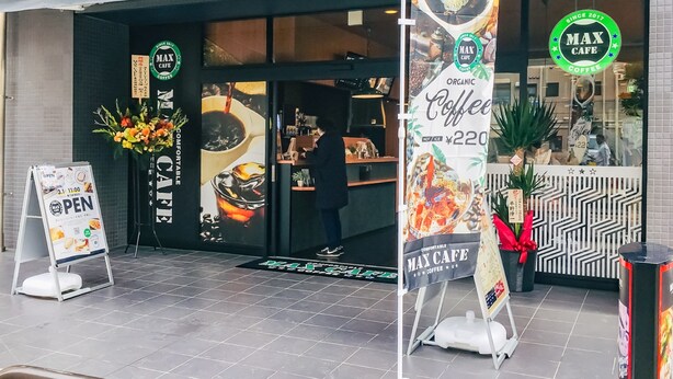 Exterior de Max Cafe, con escaparate que muestra café, un cartel grande que anuncia café orgánico y un letrero que indica que la cafetería está abierta desde 2017.