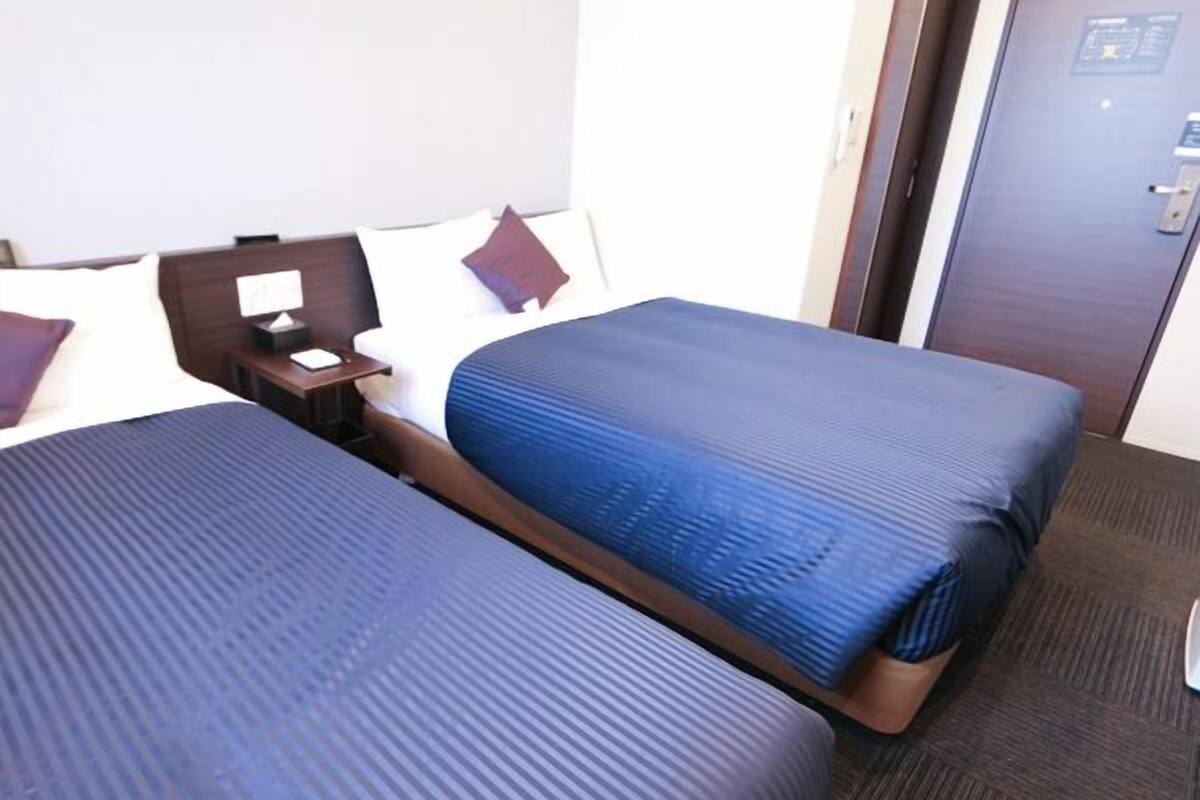 A hotel room with two beds, a nightstand, a desk, and a door.