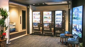 Un hall de hotel con máquinas expendedoras, zona de estar y mostrador de recepción.