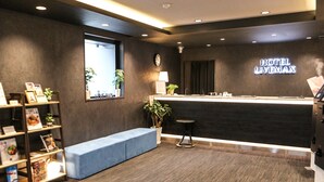Zona de recepción moderna de hotel con un mostrador de madera oscura, un banco azul y un reloj fijado a la pared.