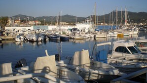 A marina with multiple boats docked, a building labeled "Ecole," and a mountainous backdrop.