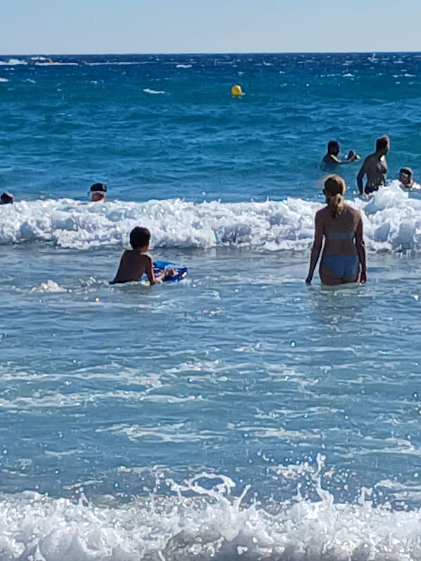 Une scène de plage où l’on voit des gens nager et jouer dans l’eau.