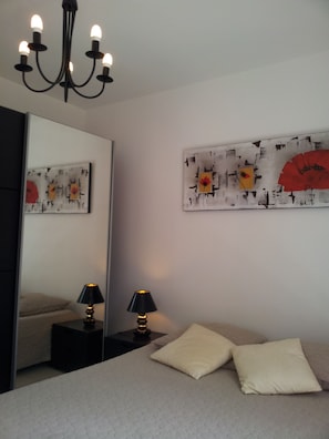Quarto com uma cama, duas mesas de cabeceira com abajures, um lustre e duas obras de arte nas paredes.