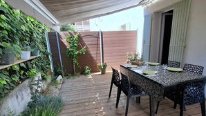 An outdoor patio with a wooden deck, a table set for dining, and a wall covered with green plants.