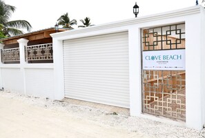 A white building with a closed garage door and a sign reading "CLOVE BEACH GUEST HOUSE." - Clove Beach (Feydhoo)