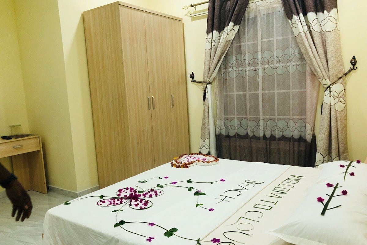 A bedroom with a bed, a wardrobe, a desk, and a window with curtains.