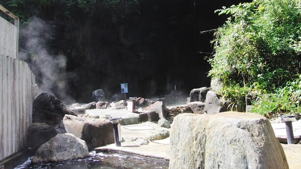 Zona de aguas termales con rocas, una valla de madera y un cartel.