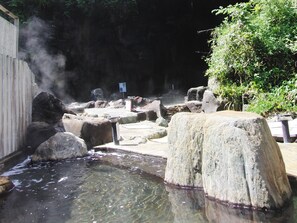 Zona de aguas termales con rocas, una valla de madera y un cartel.