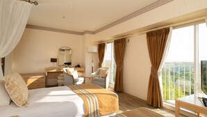 Habitación de hotel con cama, escritorio, silla, mesita y balcón con vistas.