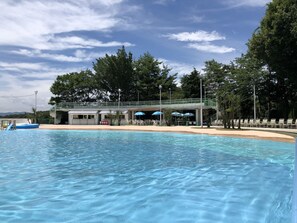 Una piscina con agua cristalina, rodeada de árboles y una zona cubierta con sombrillas.