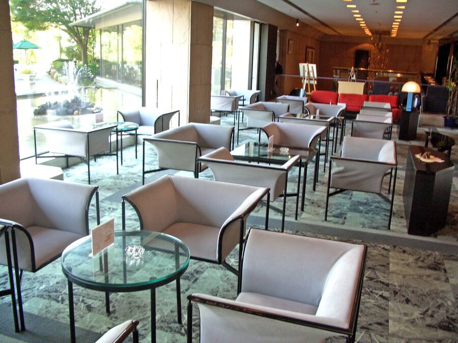 A spacious indoor area with multiple tables and chairs, large windows offering a view of the outdoors, and a stage with musical instruments in the background.