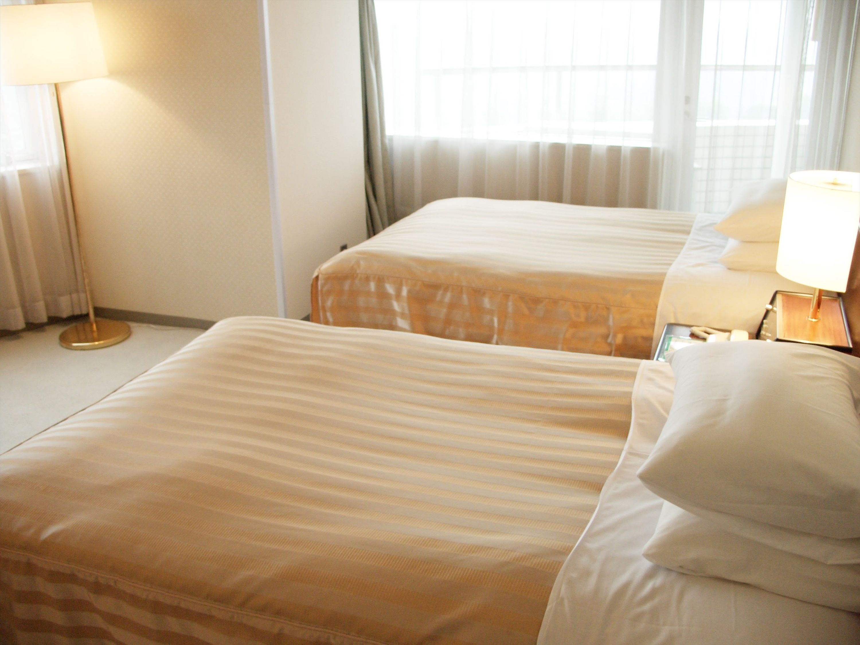A hotel room with two beds, a bedside table with a lamp, and a window with curtains.