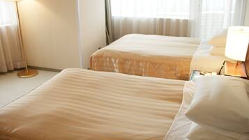 A hotel room with two beds, a bedside table with a lamp, and a window with curtains.