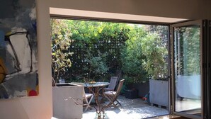 Ein modernes Wohnzimmer mit einem großen Glasfenster, das in einen Garten führt. Es gibt einen Esstisch mit Stühlen, ein Sofa und einen Couchtisch.