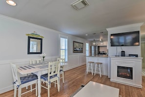 A dining area with a white table and chairs, a fireplace, and a kitchen with a TV. - Steps to Beach! 'Surf Cottage' in Galveston (Galveston)