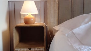 A corner of a room with a wooden nightstand, a lamp, and a bed.