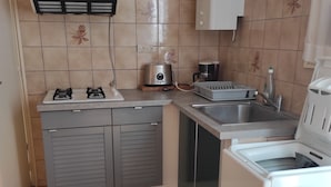 Een kleine keuken met een gasfornuis, een broodrooster, een spoelbak en een wasmachine.