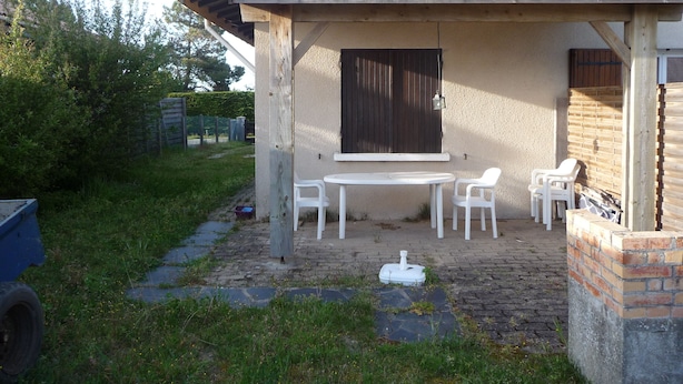 Een overdekt terras met een tafel, stoelen, een raam en een bakstenen muur.