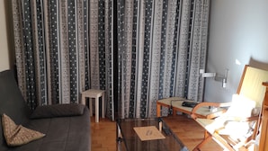 Een woonkamer met een bank, een glazen salontafel, een houten stoel en behang met patroon.