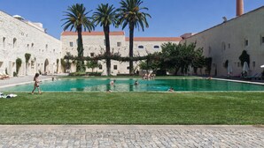 Una piscina envoltada d'edificis de pedra amb palmeres, un cel clar i una xemeneia de maó.