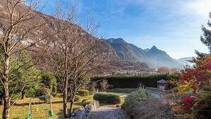 A stone pathway leading to a swing set in a mountainous area with a view of a town in the distance.