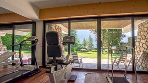 A gym with exercise equipment, large windows, and a view of a landscaped outdoor area.
